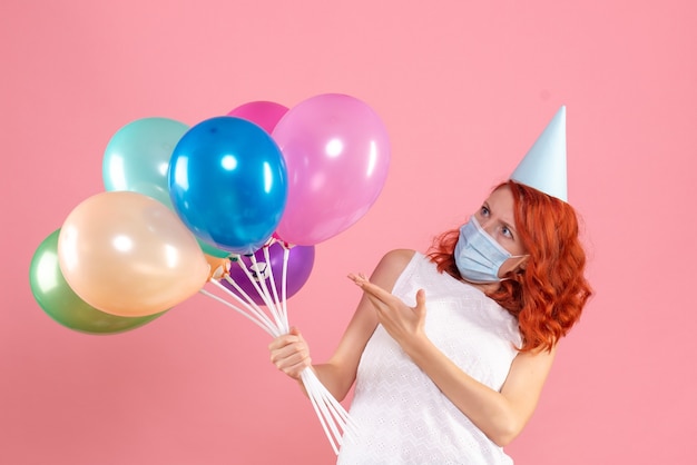 Free photo front view of young woman holding colorful balloons in sterile mask on pink wall