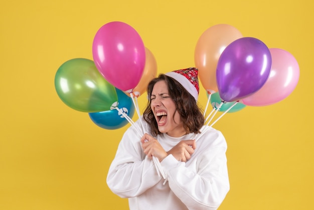 Front view of young woman holding colorful balloons on yellow wall