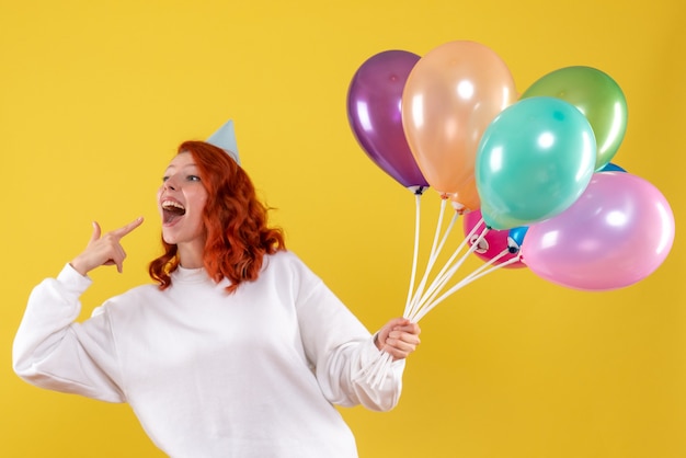 Free photo front view of young woman holding colorful balloons on yellow wall