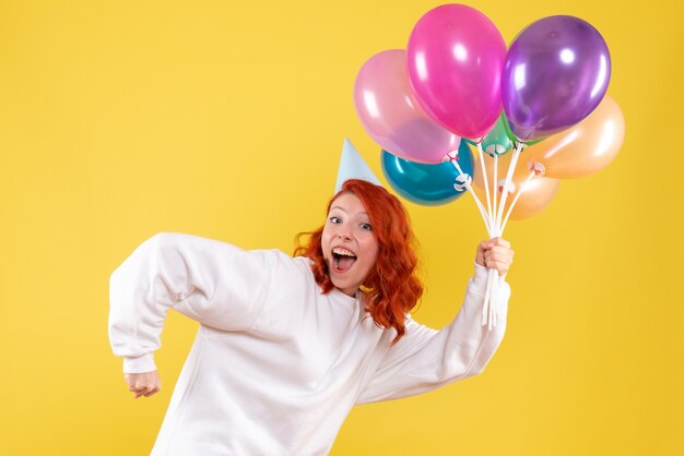 Free photo front view of young woman holding colorful balloons on yellow wall