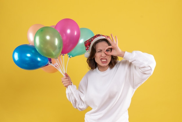 Free photo front view young woman holding colorful balloons on yellow