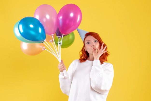 Free photo front view of young woman holding cute colorful balloons on yellow wall