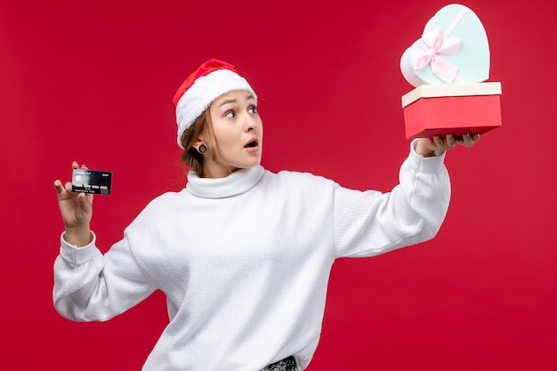 Free photo front view young woman holding gifts and bank card on red background