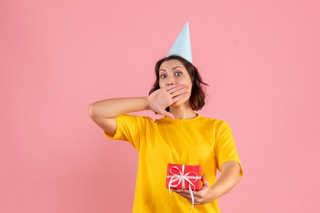 Front view of young woman holding little present on a pink wall