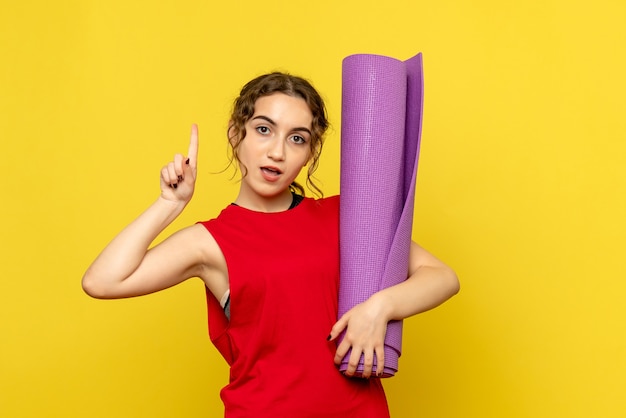 Front view of young woman holding purple carpet on light yellow wall