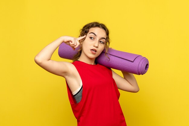 Front view of young woman holding purple carpet on a yellow wall