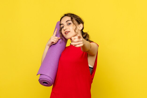 Front view of young woman holding purple carpet on a yellow wall