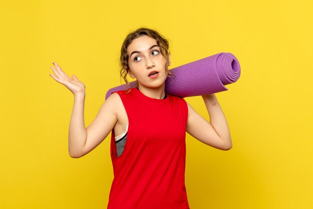 Front view of young woman holding purple carpet on the yellow wall