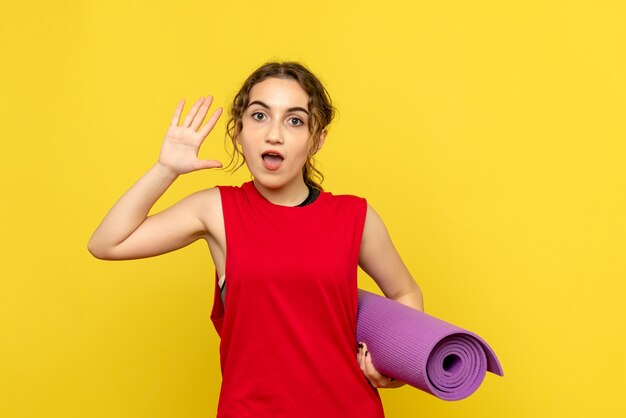 Front view of young woman holding purple carpet on yellow wall