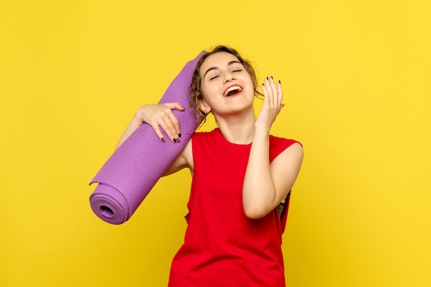 Front view of young woman holding purple carpet on yellow wall