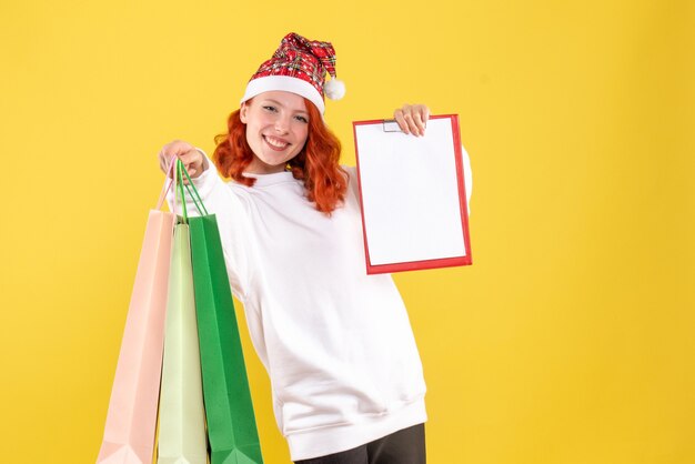 Front view of young woman holding shopping packages on yellow wall