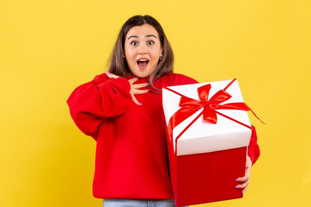 Front view young woman holding xmas gift on a yellow background