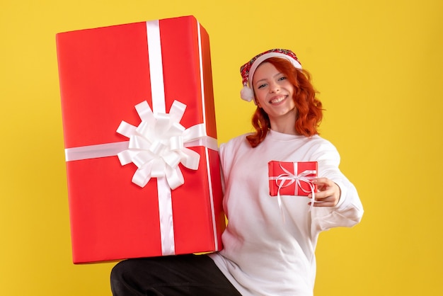 Free photo front view of young woman holding xmas presents on yellow wall