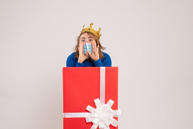 Front view of young woman inside gift box in mask calling on white wall