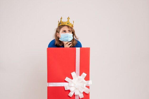 Front view of young woman inside gift box in mask on a white wall