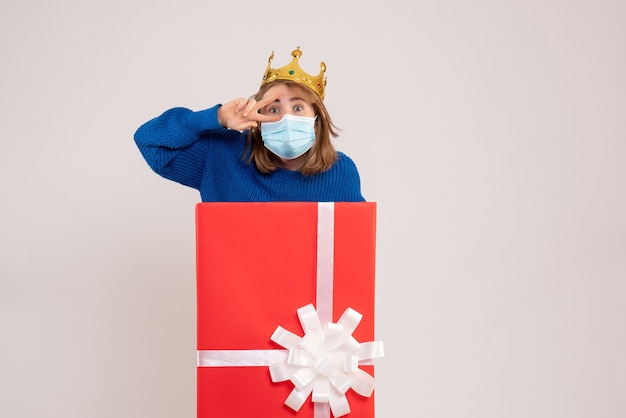 Front view of young woman inside gift box in mask on white wall