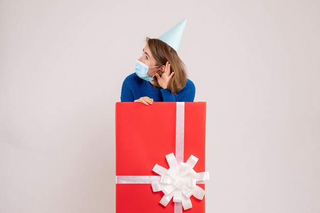 Front view of young woman inside present box in mask on a white wall