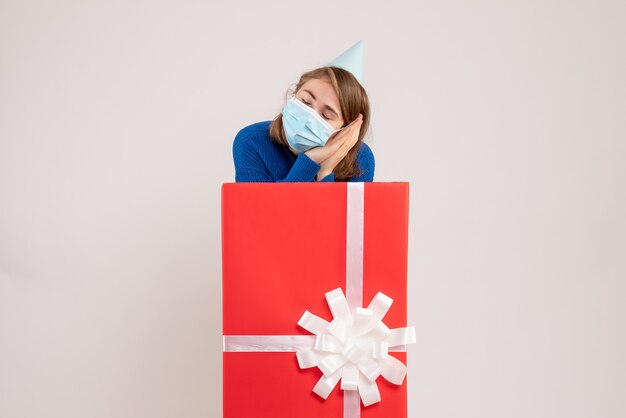 Front view of young woman inside present box in mask on white wall