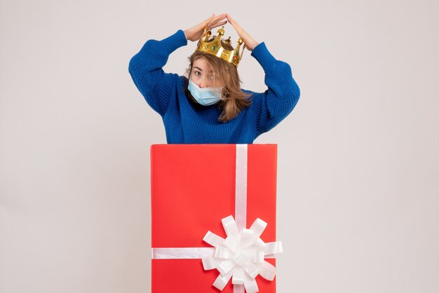 Front view of young woman inside present box in mask on white wall