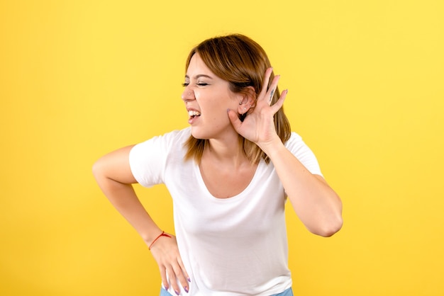 Front view of young woman listening on yellow wall