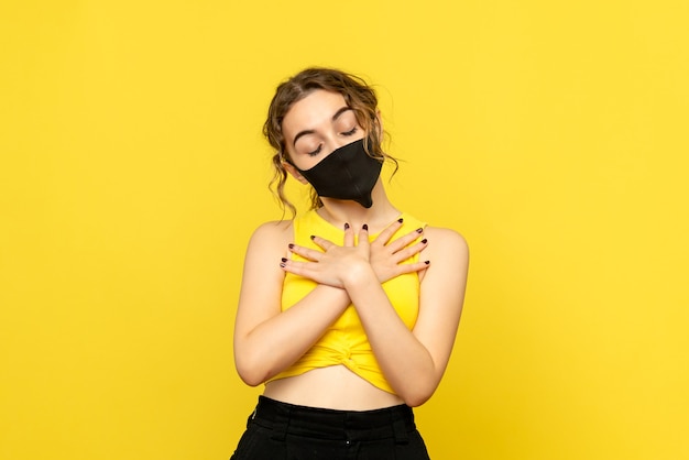 Front view of young woman in mask on yellow wall