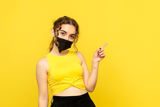 Front view of young woman in mask on yellow wall