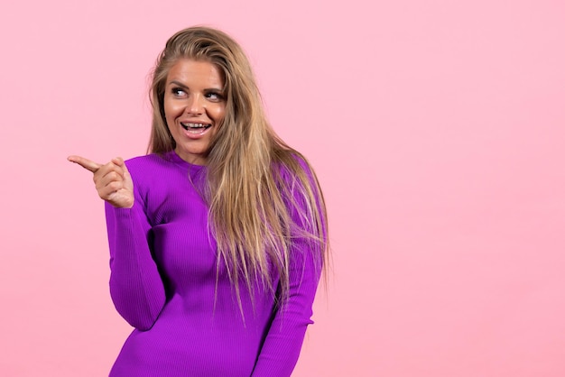 Front view of young woman posing in beautiful purple dress on light pink wall