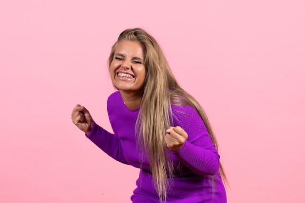 Front view of young woman posing and rejoicing in beautiful purple dress on pink wall