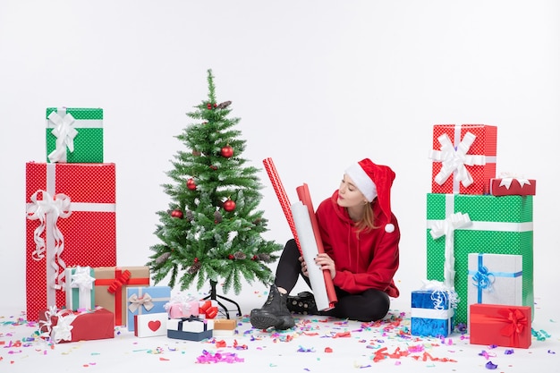 Front view of young woman sitting around holiday presents on a white wall