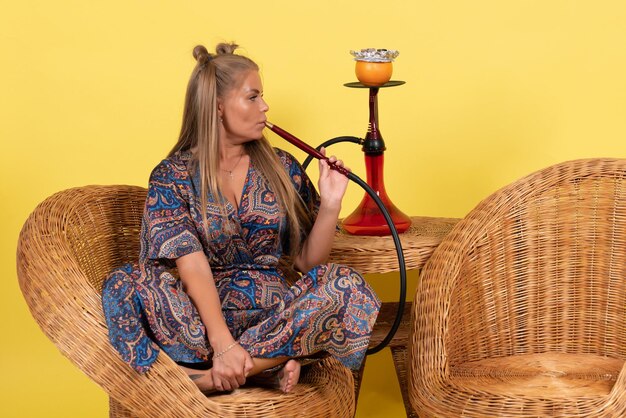 Front view of young woman smoking hookah on the yellow wall