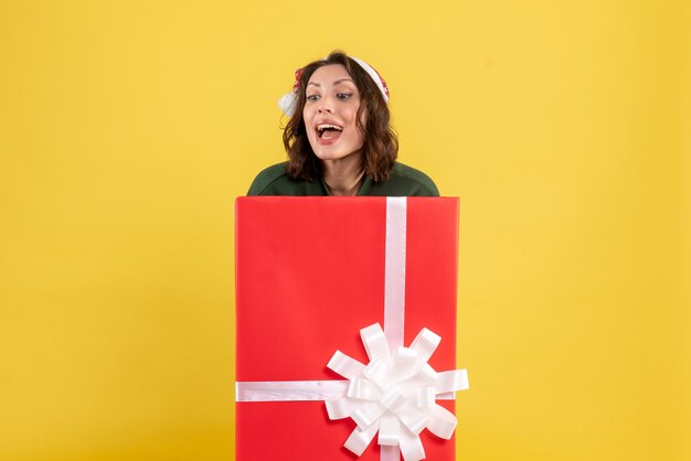 Front view of young woman standing inside box on yellow wall