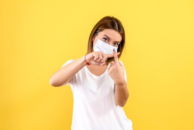 Front view of young woman in sterile mask on a yellow wall