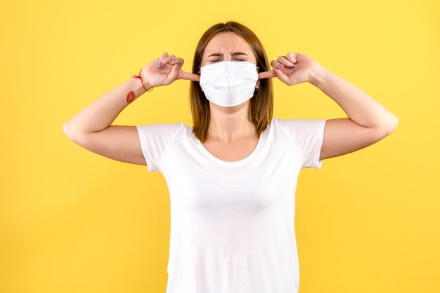 Front view of young woman stucking her ears on yellow wall