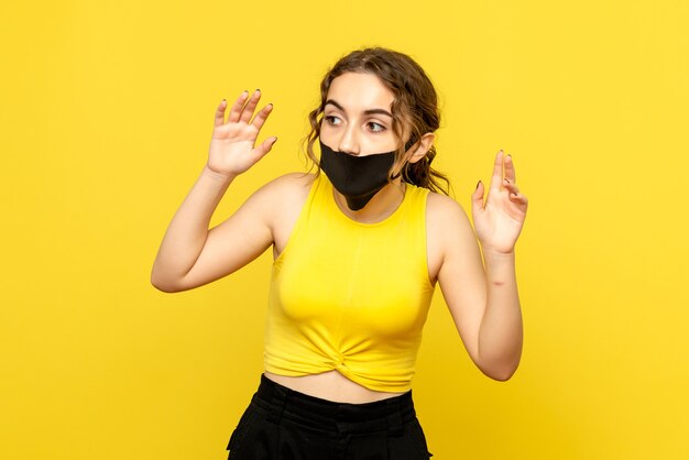 Front view of young woman with black mask on yellow wall