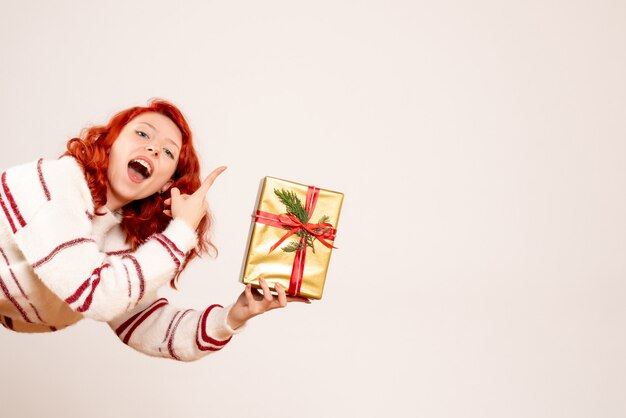 Front view of young woman with christmas present on white wall