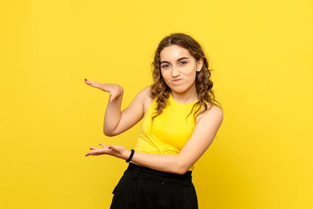 Front view of young woman with confused expression on a yellow wall