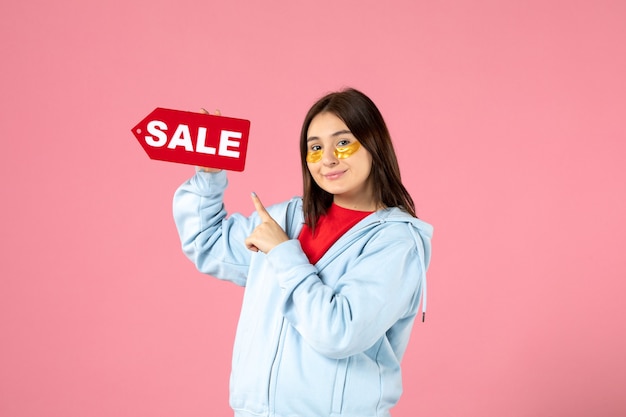 Free Photo front view of young woman with eye patches holding sale banner on pink wall