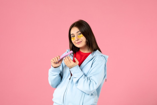 front view of young woman with eye patches and nail file on pink wall