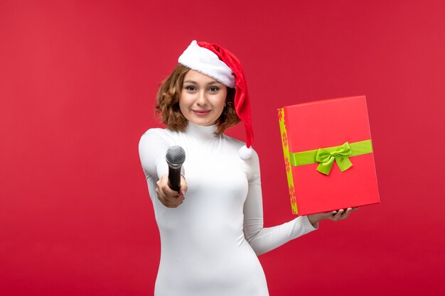 Front view of young woman with present and mic on red