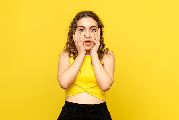 Front view of young woman with surprised expression on yellow wall