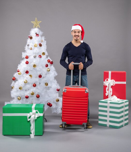 Front view young xmas man with santa hat standing near xmas tree on grey isolated 