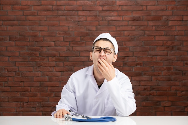 Free Photo front view young yawning doctor in white medical suit on brown brick wall