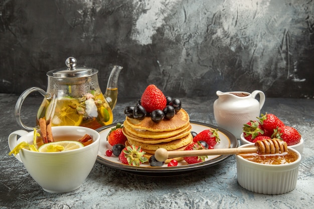 Front view yummy pancakes with fruits and tea on light surface sweet fruits breakfast