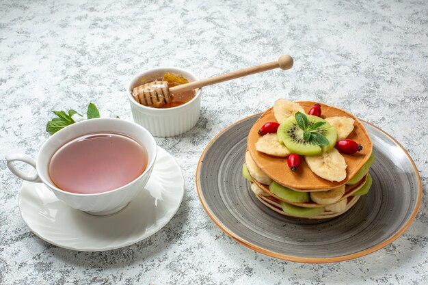 Front view yummy pancakes with sliced fruits and cup of tea on white surface fruit sweet dessert sugar breakfast color cake