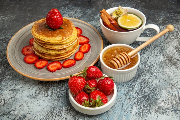 Front view yummy pancakes with strawberries and cup of tea on light surface cake fruit sweet