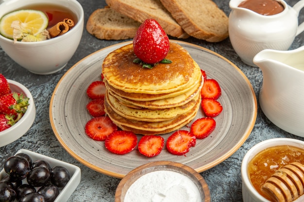 Front view yummy pancakes with tea and fruits on the light surface fruit cake sweet