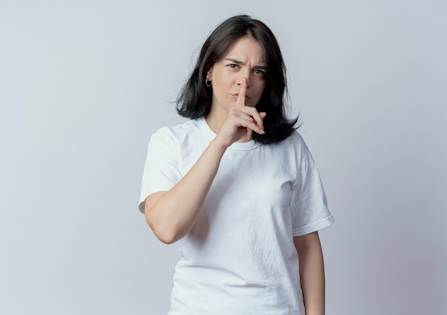 Frowning young pretty caucasian girl gesturing silence at camera isolated on white background with copy space