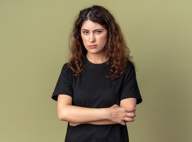 Frowning young pretty girl standing with closed posture  isolated on olive green wall with copy space