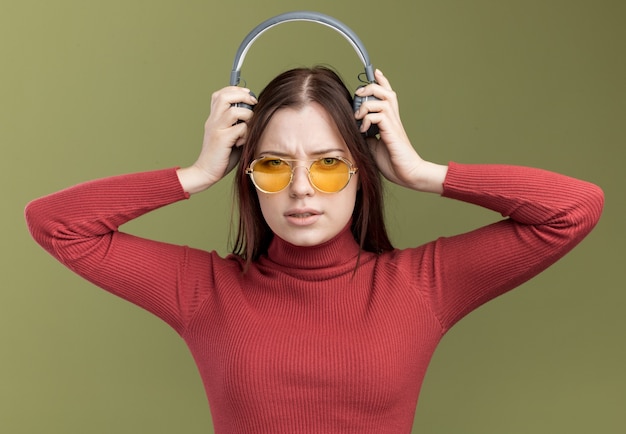 Free Photo frowning young pretty girl wearing sunglasses taking headphones off 