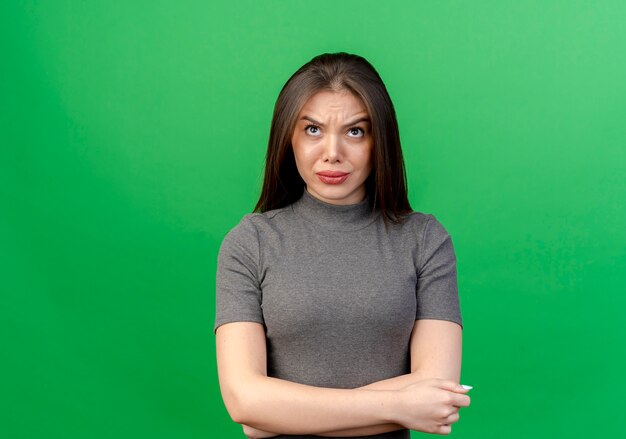 Frowning young pretty woman standing with closed posture and looking up isolated on green background with copy space